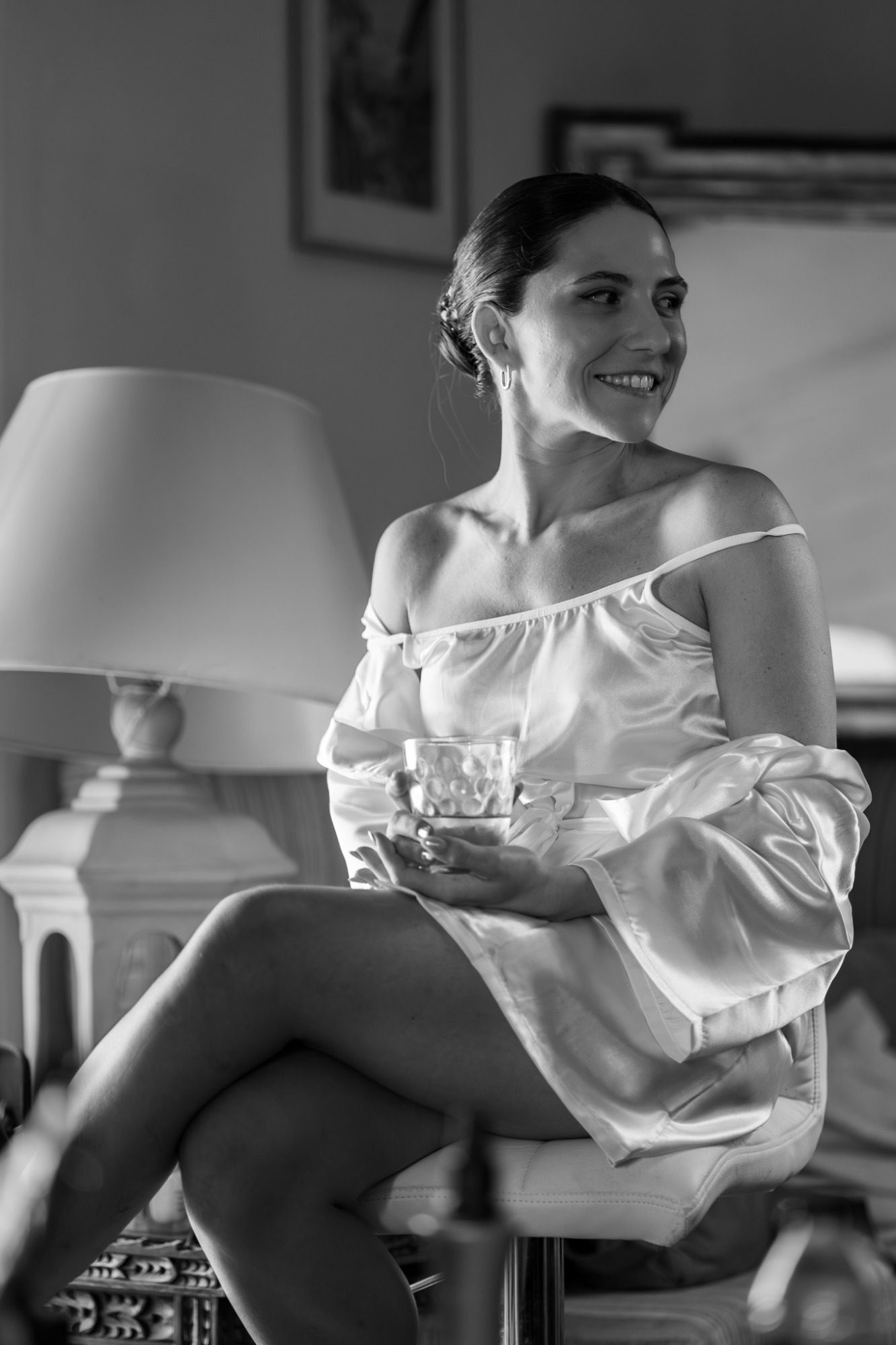 Mujer sonriente sentada en una silla, vestida con una blusa blanca y en un ambiente elegante.