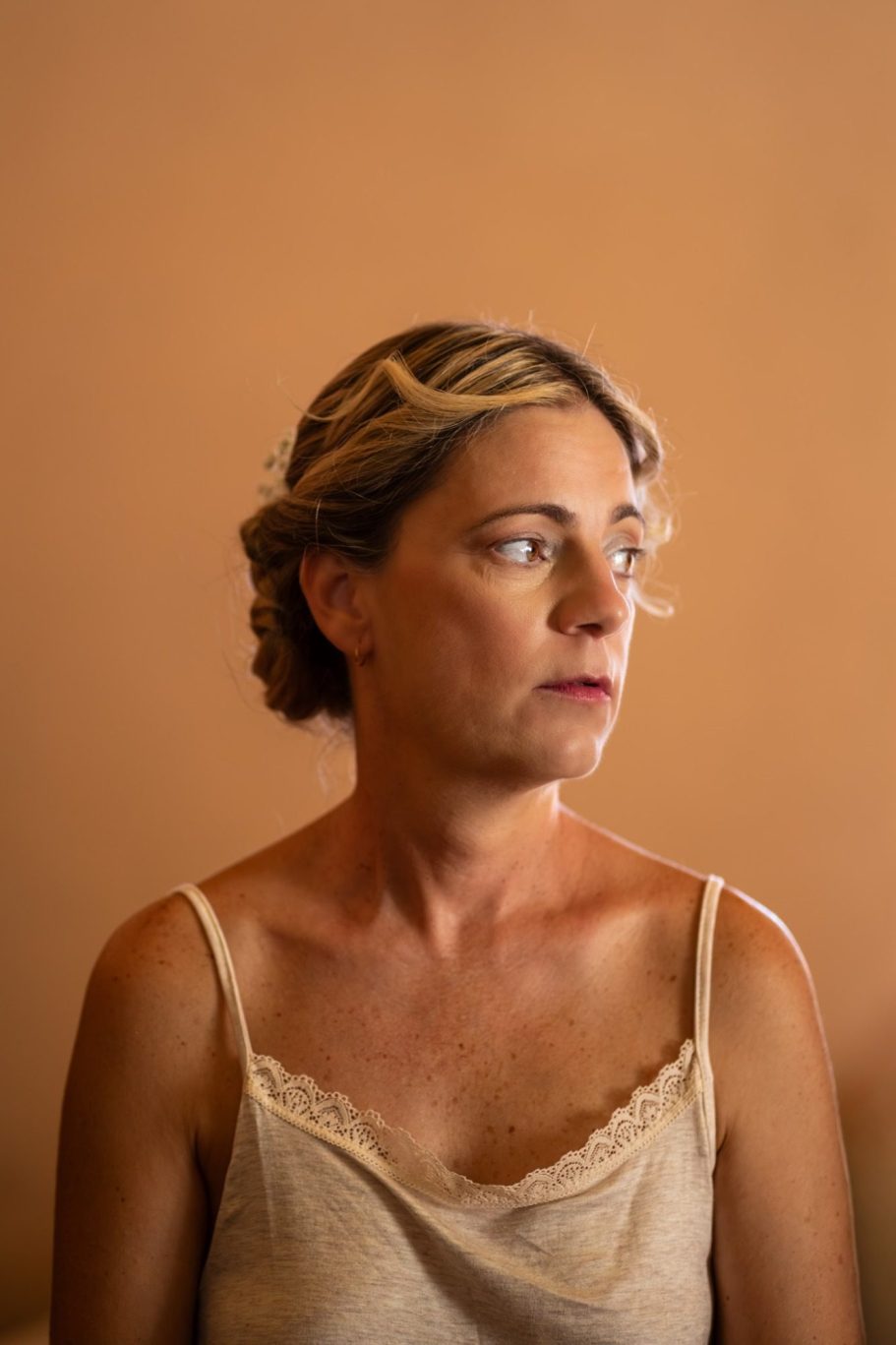 Mujer de cabello rizado con trenza, mirada pensativa, fondo naranja suave.