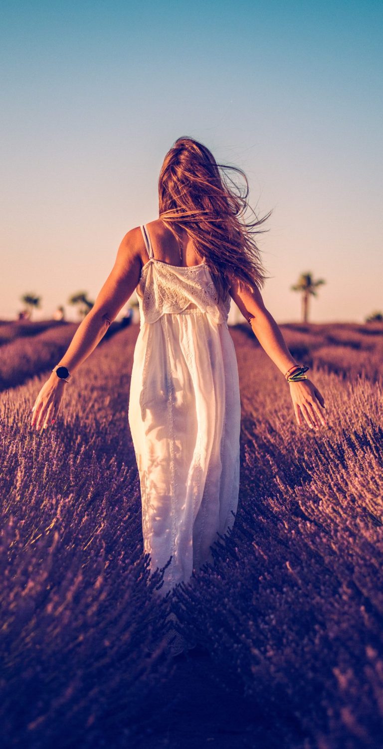 Mujer de espaldas caminando por un campo de lavanda al atardecer.