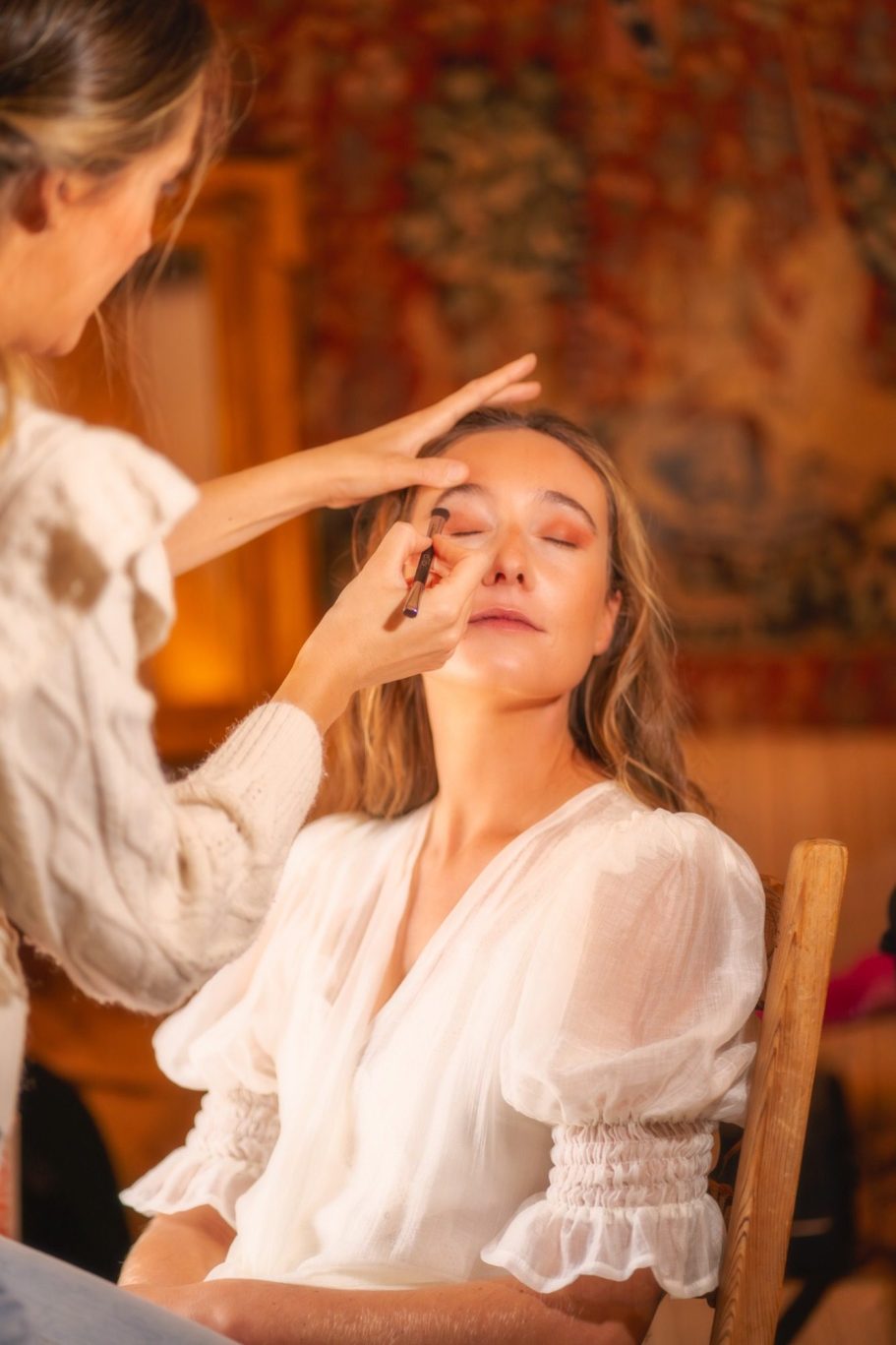 Una mujer recibe maquillaje en un entorno acogedor y cálido.