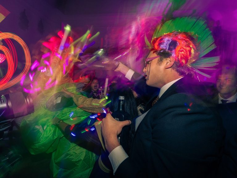 Hombres con trajes oscuros y accesorios coloridos en una fiesta animada.