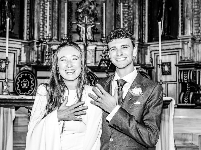 Pareja sonriente en una ceremonia, con fondo decorativo de iglesia.