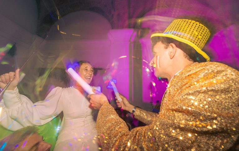 Fiesta con luces de colores, una persona con sombrero brillante y otra con vestido blanco.