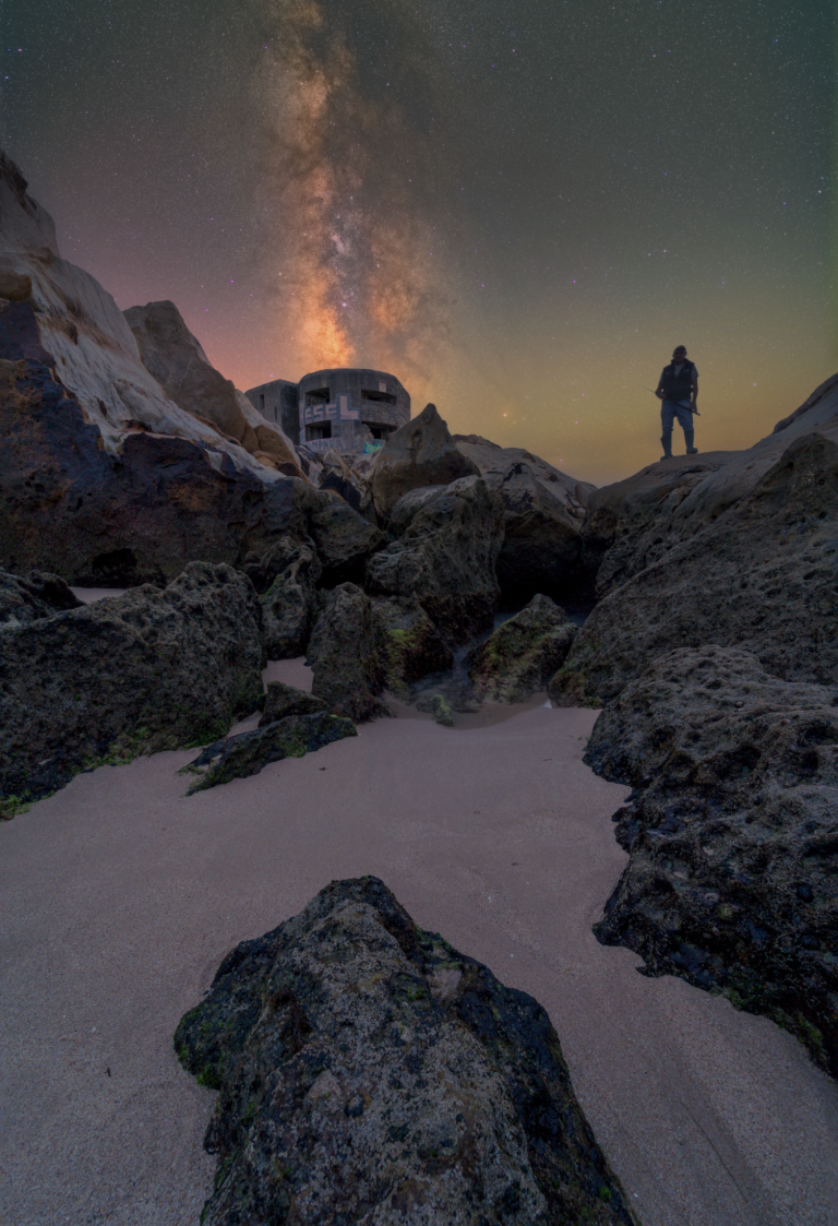 Figura solitaria sobre rocas, con la Vía Láctea iluminando el cielo nocturno.