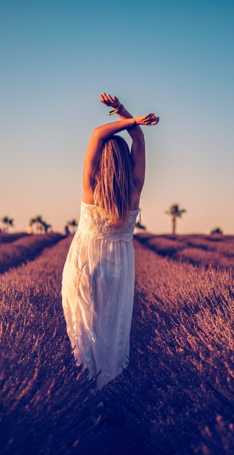 Mujer de espaldas en un campo de lavanda, levantando los brazos al atardecer.