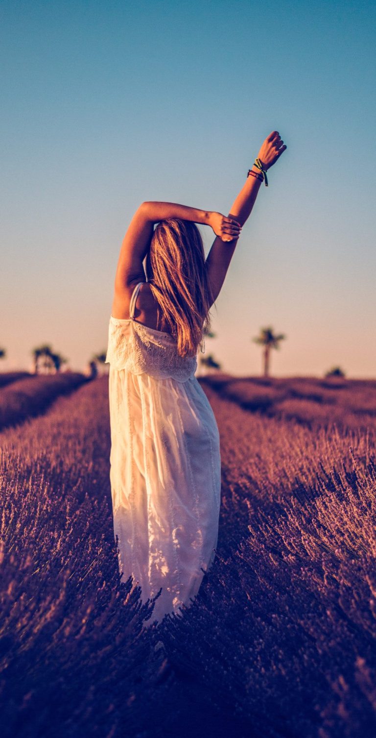 Mujer con vestido blanco, levantando un brazo, rodeada de campos de lavanda.