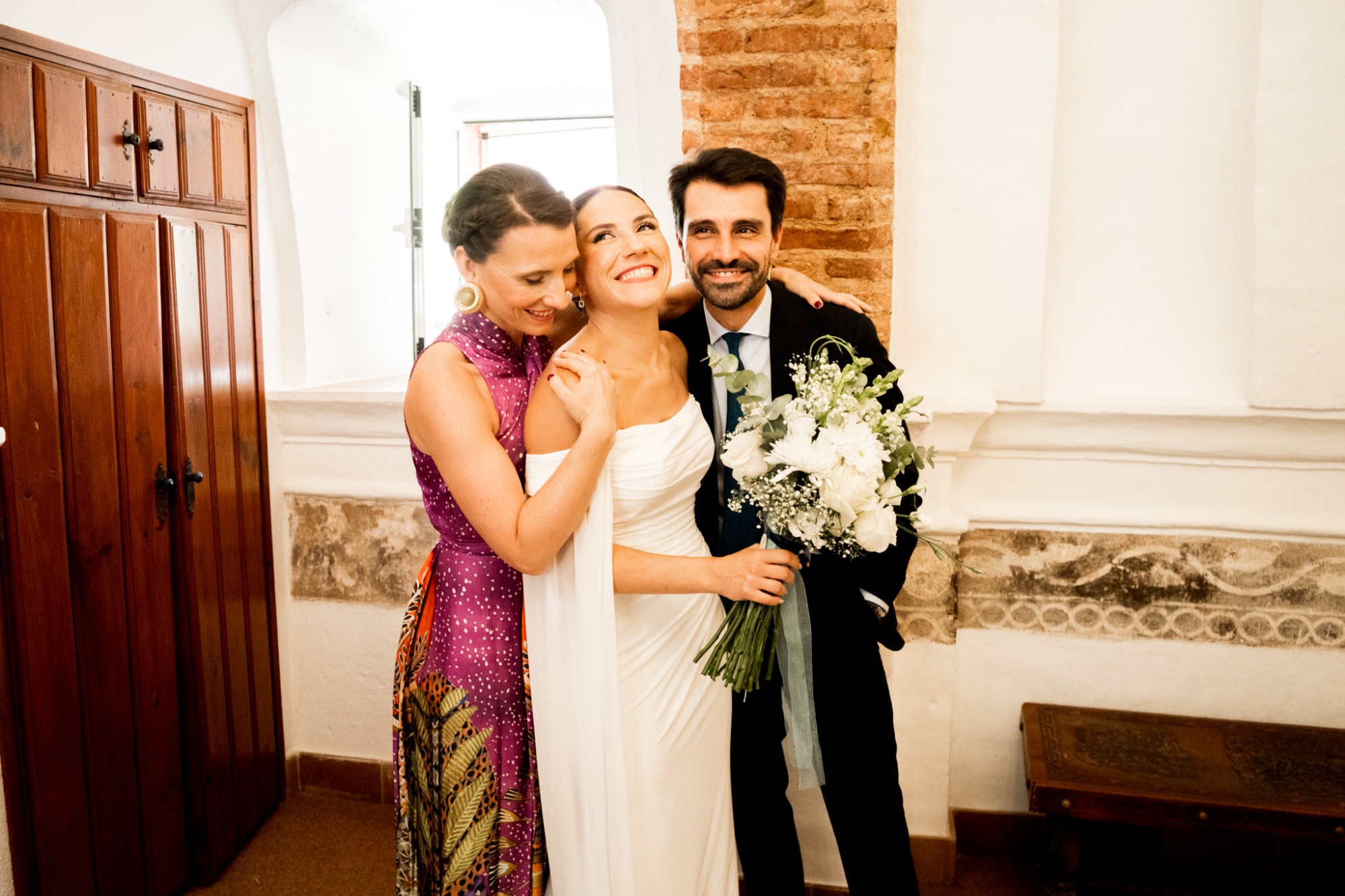 Tres personas sonrientes en un entorno festivo, con flores y vestimenta elegante.
