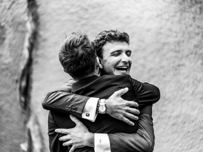 Dos hombres abrazándose con sonrisas felices, vistiéndose de traje.