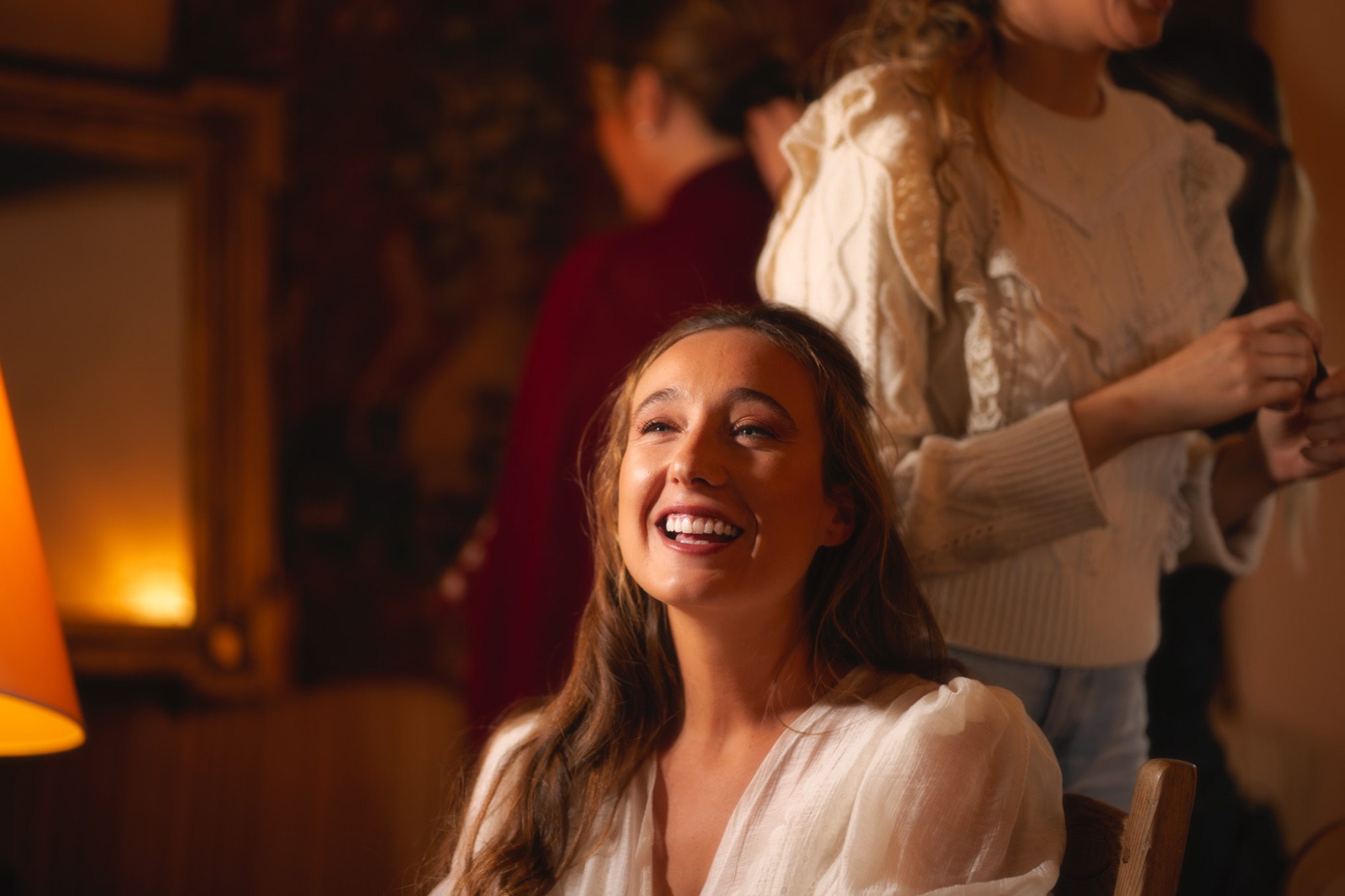 Mujer sonriente con cabello largo, iluminada por una lámpara en un ambiente festivo.